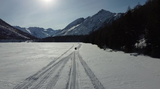 Drone aerial footage of a snowmobile riding across a frozen lake and snowy terrain in Russia. Captured from various angles, this footage highlights winter adventure, remote wilderness