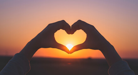 Silhouette of hands making a heart shape against a sunset.







