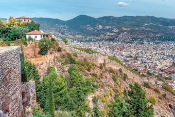 A scenic view of Alanya Castle's stone walls stretching along the mountainside, overlooking the city of Alanya, Turkey. The castle offers a breathtaking panorama of the surrounding landscape