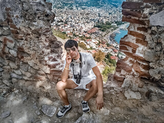 Tourist with camera resting within the ancient ruins of Alanya Castle, Turkey, while enjoying a breathtaking view of the city and harbor. The scene highlights both history and modern tourism