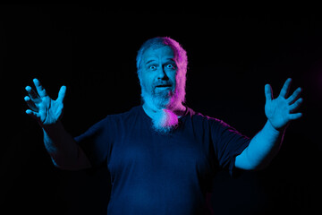 A bearded man with an open hand gesture, as if explaining, lit by blue and purple neon lights