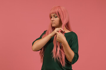 a woman in a green dress on a pink background weaves a pigtail out of her pink hair