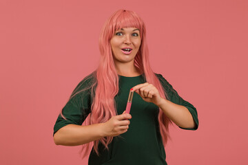 cheerful woman in a pink wig with her mouth open looking at the camera holding liquid lipstick