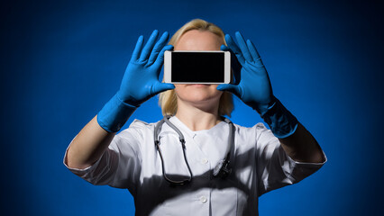 a woman doctor holds a smartphone in front of her face showing us the screen