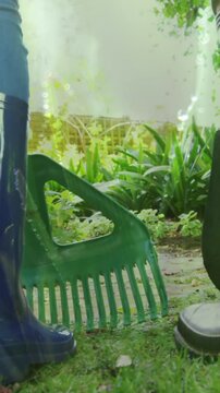 Animation of grass over legs of two people wearing rubber boots working in garden