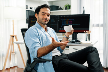 Profile's smart IT developer looking camera to pose holding coffee cup against on software...