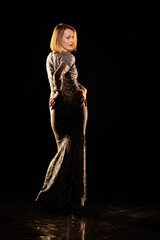 Woman in a shiny silver dress moves and dances on a black background