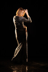 Woman in a shiny silver dress moves and dances on a black background