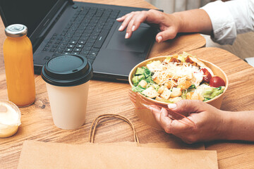 a woman is working on a laptop at home, there is food on the table, salad, coffee and juice,...