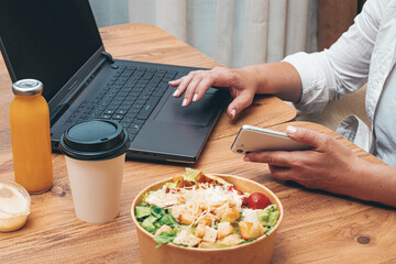 a woman is working on a laptop at home, there is food on the table, salad, coffee and juice,...