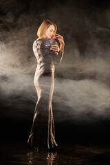 Woman in a shiny silver dress moves and dances on a black background and smoke