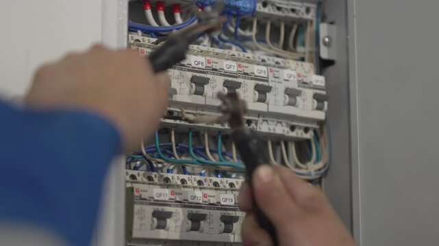 Worker checks power with amperemeter in switchboard in building closeup. Electrician hands controls network connection at construction site
