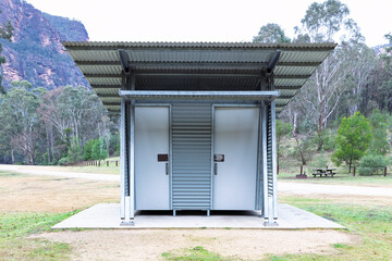 Photograph of a reasonably well maintained steel and corrugated iron unisex toilet block on a concrete base located in a large public use campground facility.