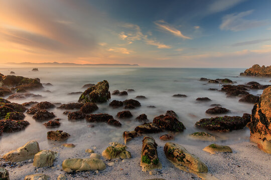 View of the rocky shoreline with soft light on the water creating a dreamy effect with gentle waves lapping against the rocks, Hermanus, Western Cape, South Africa.