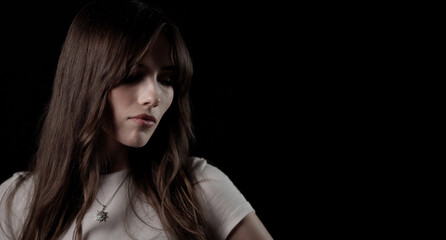 Studio portrait of a young woman with long brown hair wearing white t shirt and pendant necklace...