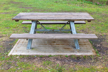 Photograph of a fixed in place reasonably well maintained family sized wood and steel picnic table with adequate seating located in a large public use campground facility.