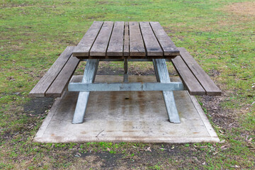 Photograph of a fixed in place reasonably well maintained family sized wood and steel picnic table with adequate seating located in a large public use campground facility.