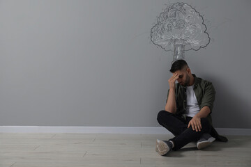 Worried man sitting on floor. Confused thoughts depicted by explosion on grey wall behind him....