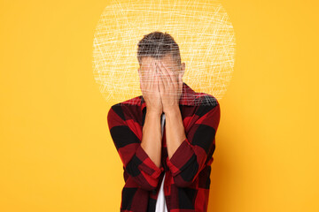 Worried man covering his eyes on orange background. Confused thoughts as messy lines around his...