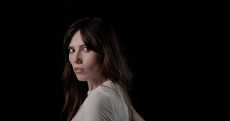 Portrait of a beautiful young woman with long brown hair looking over her shoulder against a black...