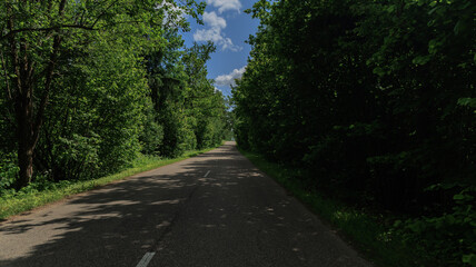 Obraz premium Road in the countryside, roadside and asphalt, green forest and fields, blue sky and clouds 