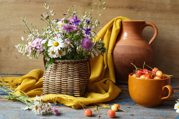 Summer still life: a bouquet of wild flowers in a basket with clay dishes and ripe cherries