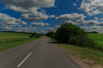 Road in the countryside, roadside and asphalt, green forest and fields, blue sky and clouds	