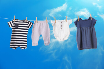 Different baby clothes drying on washing line against blue sky