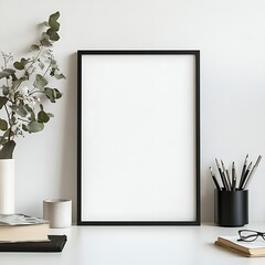 Elegant blank frame on white desk with books, stationary and plant ready for art, graphics or text additions.