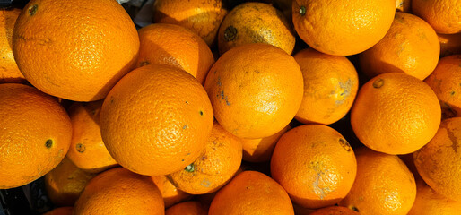 Fresh oranges with bright orange skin and natural blemishes are piled together, showing texture and vibrant color. oranges, fruit;