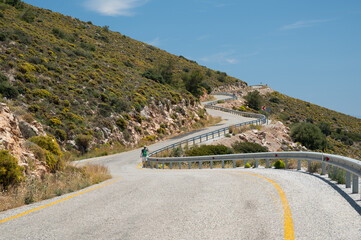 Hiker navigating a winding mountain road in Greece, enjoying the summer sun while embracing the...