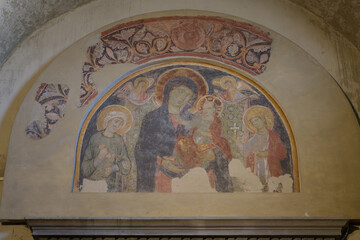 Medieval fresco of Virgin Mary and baby Jesus with haloed saints and angels under an ornamental...