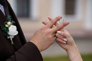 Wedding Rings Exchange Ceremony Symbolizing Love and Commitment, Brown Suit, White Roses, Hands Interlocked, Building Backdrop, Romantic Style