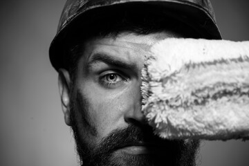 Closeup portrait of painter with paint roller. Painter in hard hat covering eye with painting...