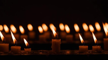 Rows of lit candles with somber mood, representing remembrance, against a dark background 