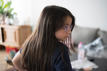 Smiling girl in glasses and t-shirt in a messy room. Concept: carefree childhood, authenticity, joyful innocence, playful environment.