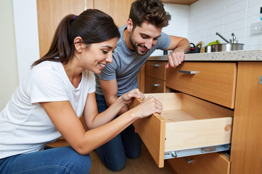 Happy young couple working together as a team to assemble a new wooden kitchen drawer, smiling while doing a DIY home improvement project in their modern apartment