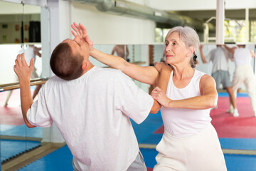 Senior European woman learning chin strike move on man during self-defense training.