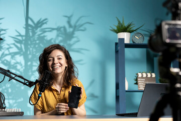 Joyful influencer presents smartphone from sponsoring brand, analyzing features. Upbeat content...