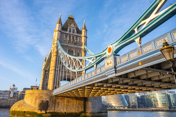 Obraz premium Early morning sunlight illuminates Tower Bridge, creating a stunning view over the Thames River. The iconic structure blends history with the vibrant atmosphere of London.