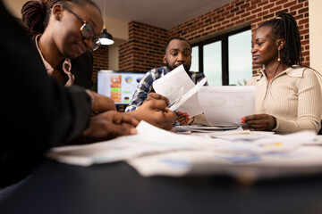 African american colleagues gathered around table, reviewing multiple documents during startup...