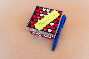 Thank you note that says thank you handwritten with blue pen with a background of a gift box with...