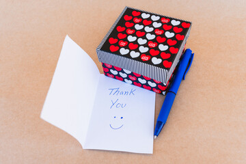 Thank you note that says thank you handwritten with blue pen with a background of a gift box with...