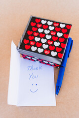 Thank you note that says thank you handwritten with blue pen with a background of a gift box with red and white hearts