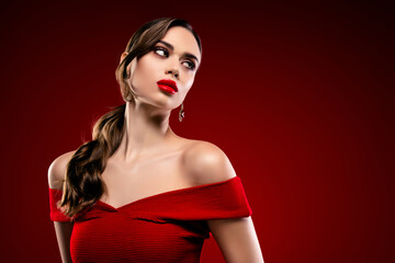 Elegant young woman wearing a vibrant red dress, showcasing beauty and grace against a rich red...