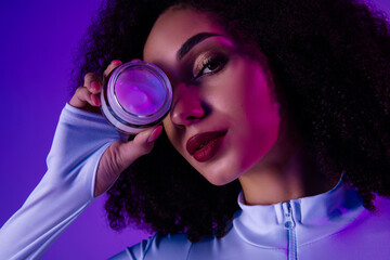 Young woman holding cosmetic product in neon light ambiance exudes glamour and style