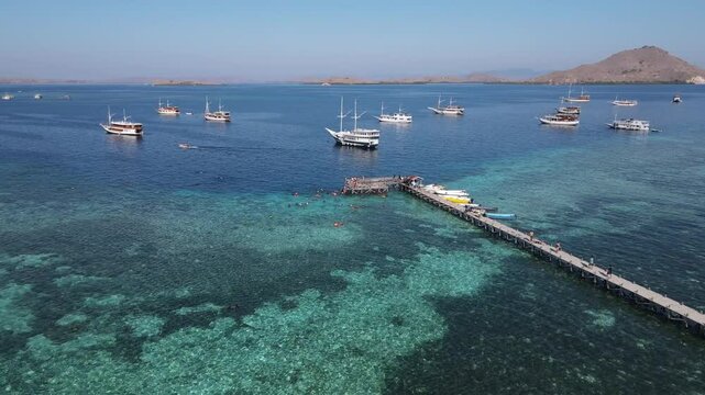 Aerial drone view of Kanawa Island beach with long bridge dock and sailing boats around.