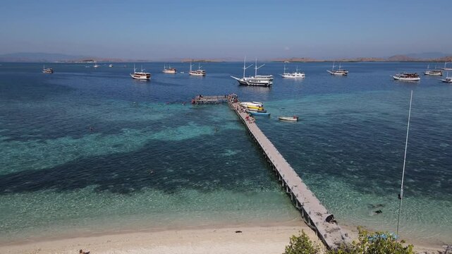 Aerial drone view of Kanawa Island beach with long bridge dock and sailing boats around.