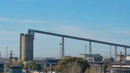 Industrial conveyor belt system leading to a tall silo structure in a factory setting under a clear...