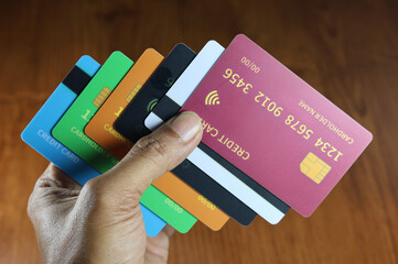 The left hand holds several dummy credit cards on a wooden patterned table.